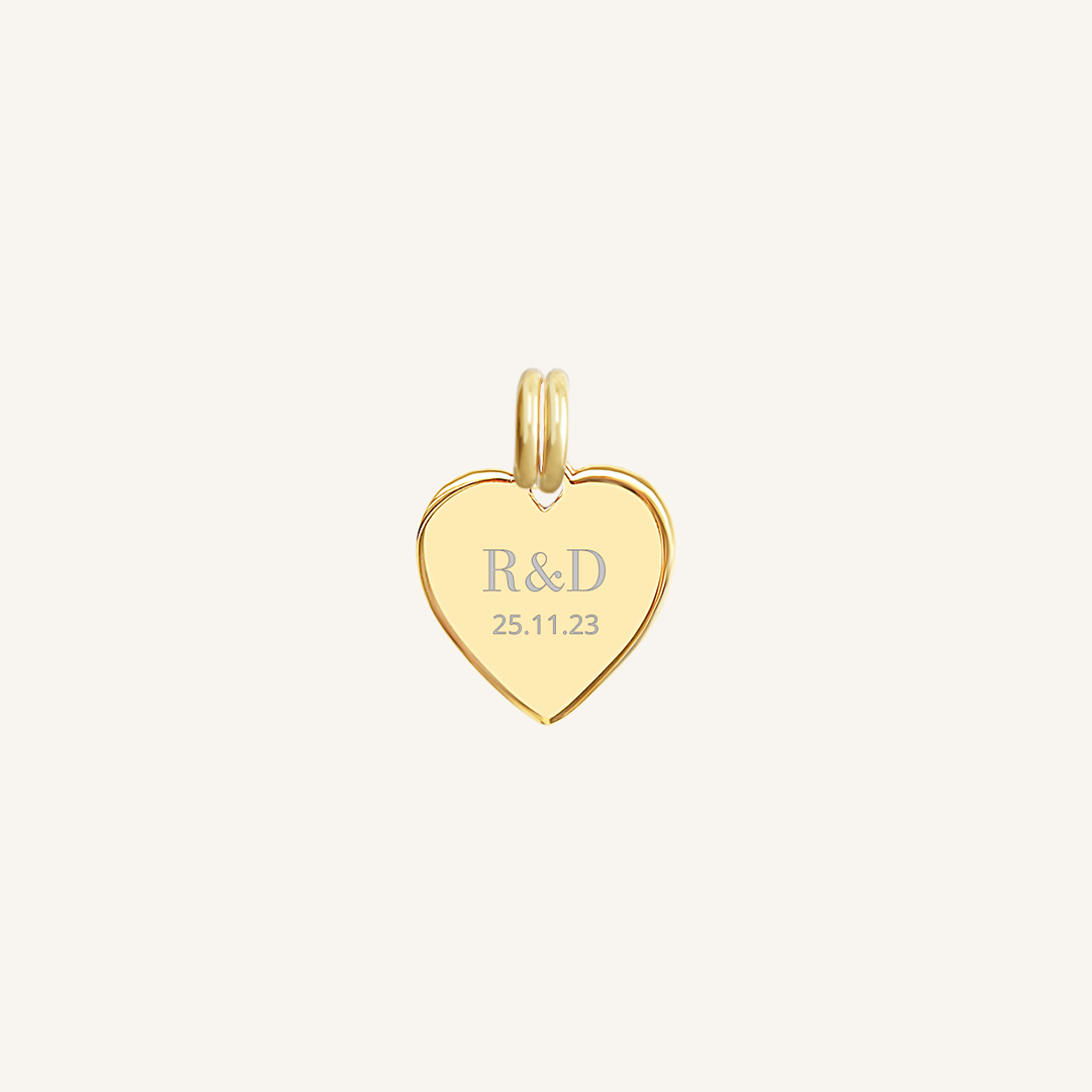 A gold heart-shaped charm with engraved initials and a date