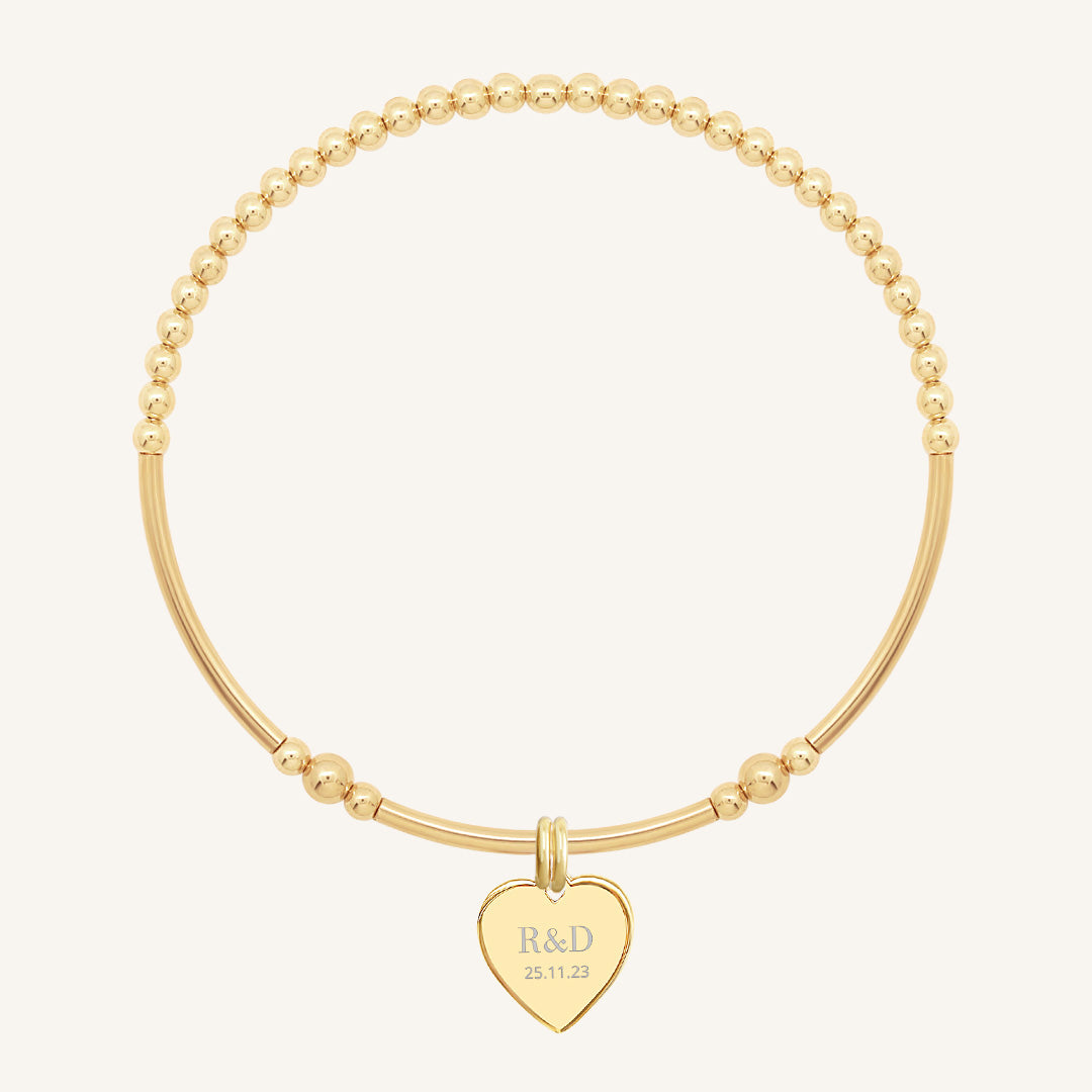 A gold bracelet with a beaded design and a heart-shaped charm, engraved with initials and a date