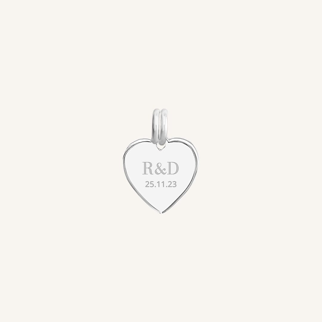 A silver heart-shaped charm with engraved initials and a date