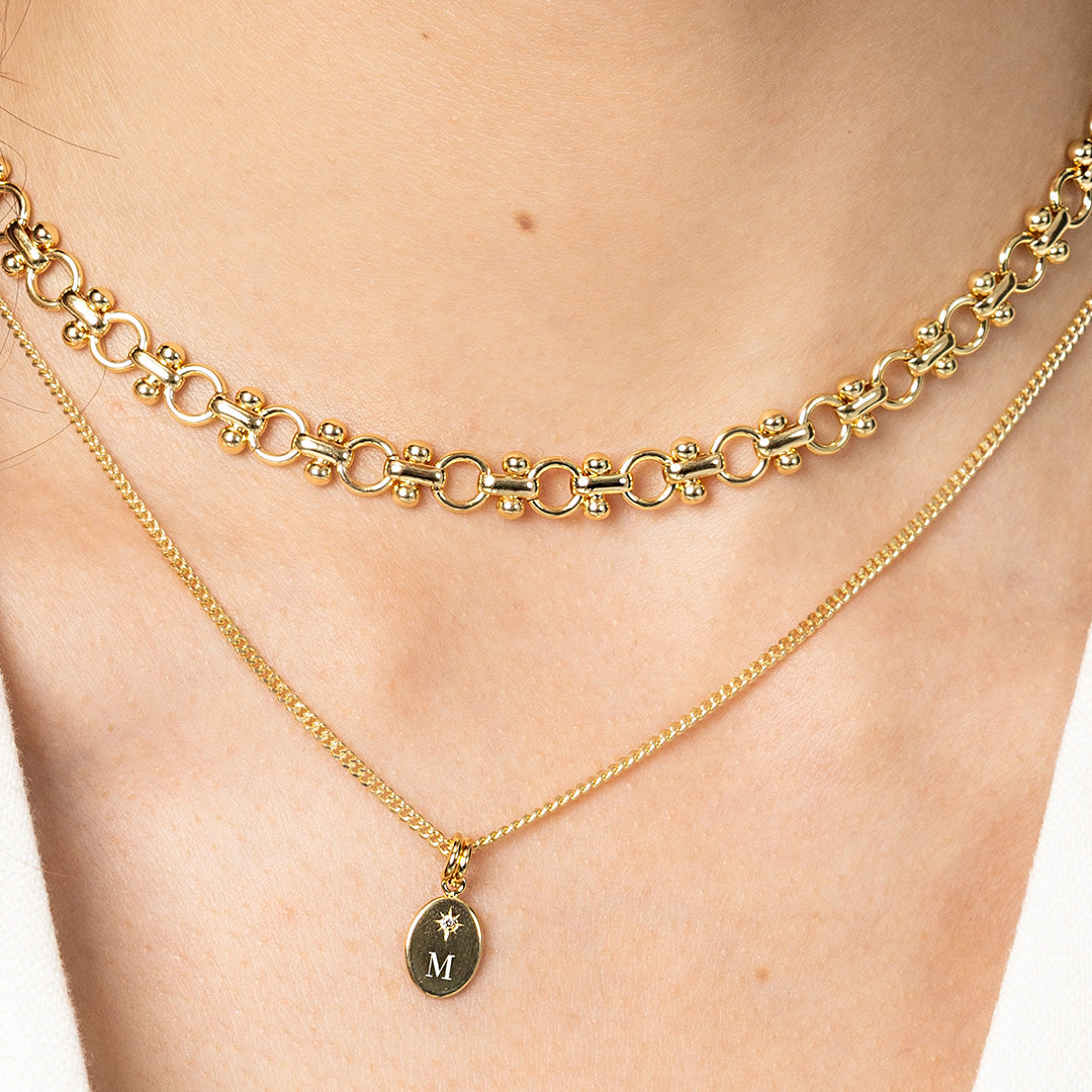 Gold chain necklace with a pendant featuring the letter 'M' on a person's neck.