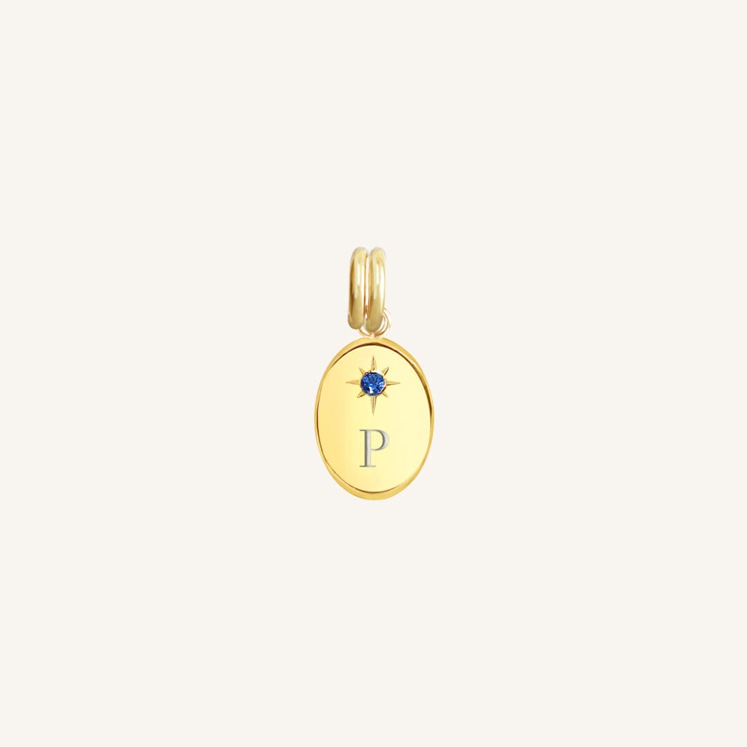 Gold pendant with a blue gemstone and letter 'P' on a light beige background