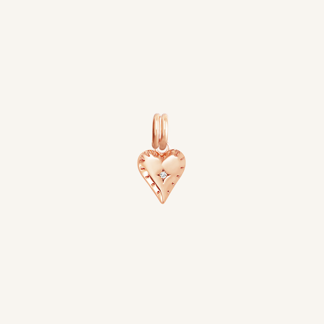 A delicate heart-shaped charm in rose metal tone, designed to be attached to a bracelet or necklace