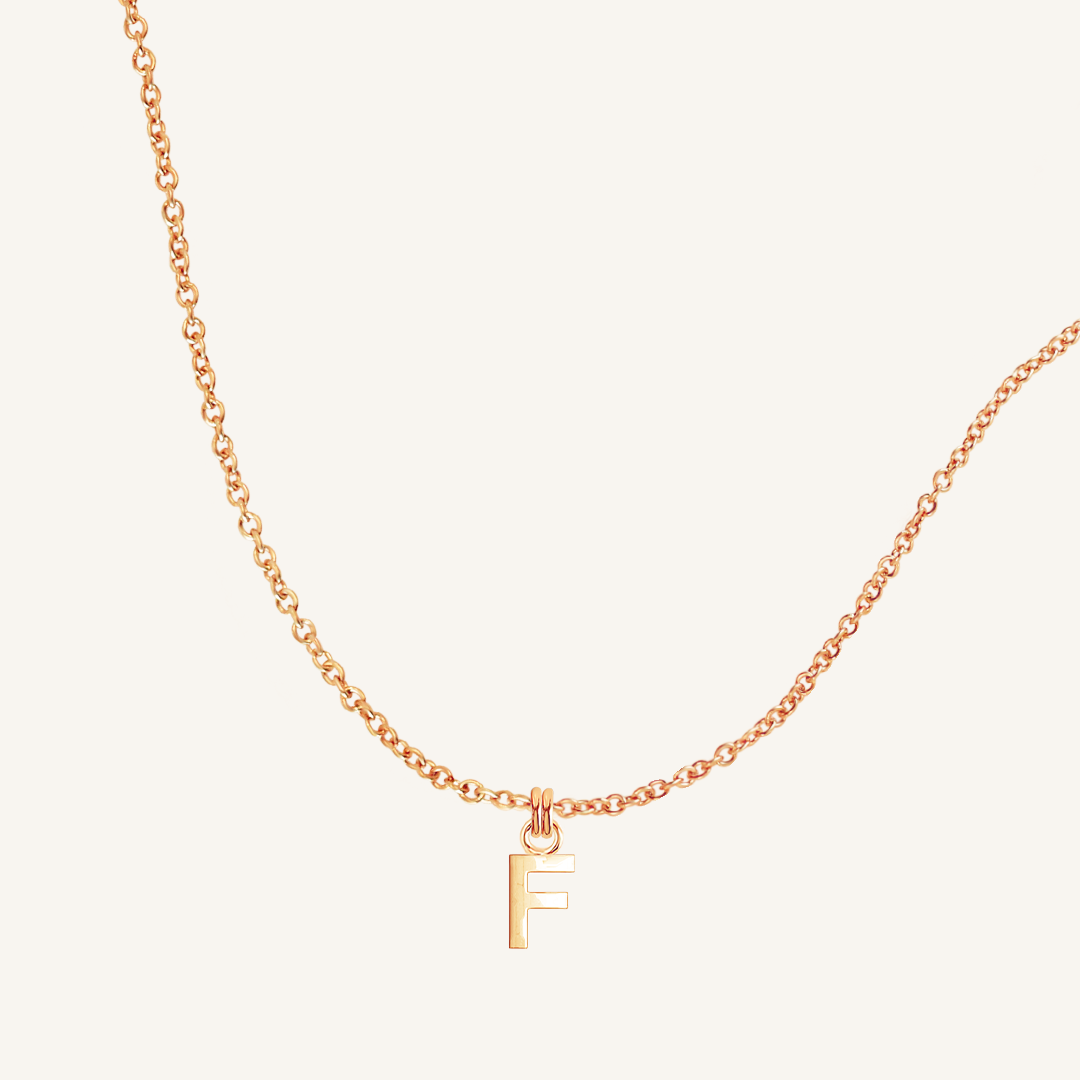 Rose gold necklace with a 'F' pendant on a light beige background