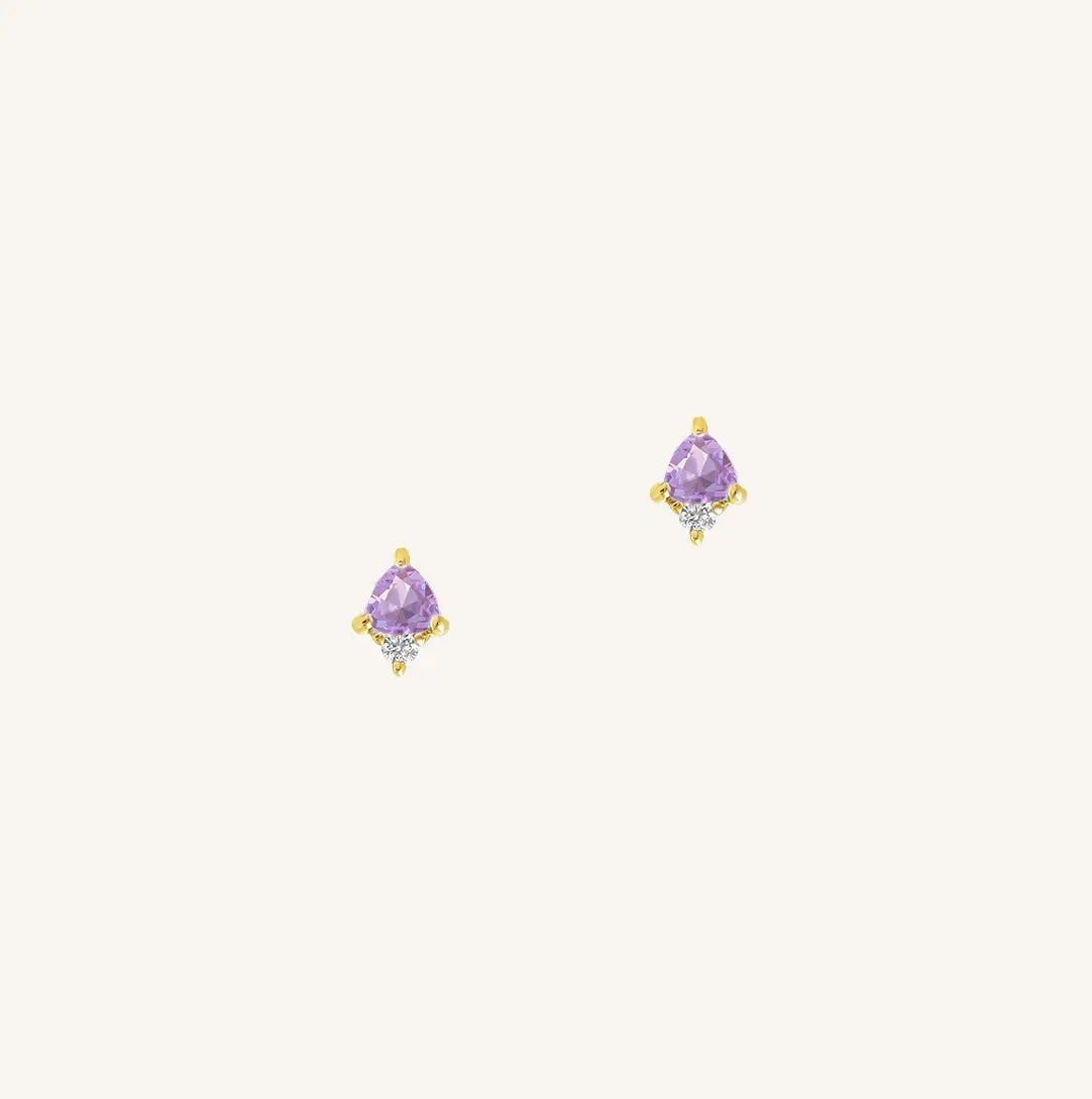 A gold pair of stud earrings featuring a purple cubic zirconia, representing February.