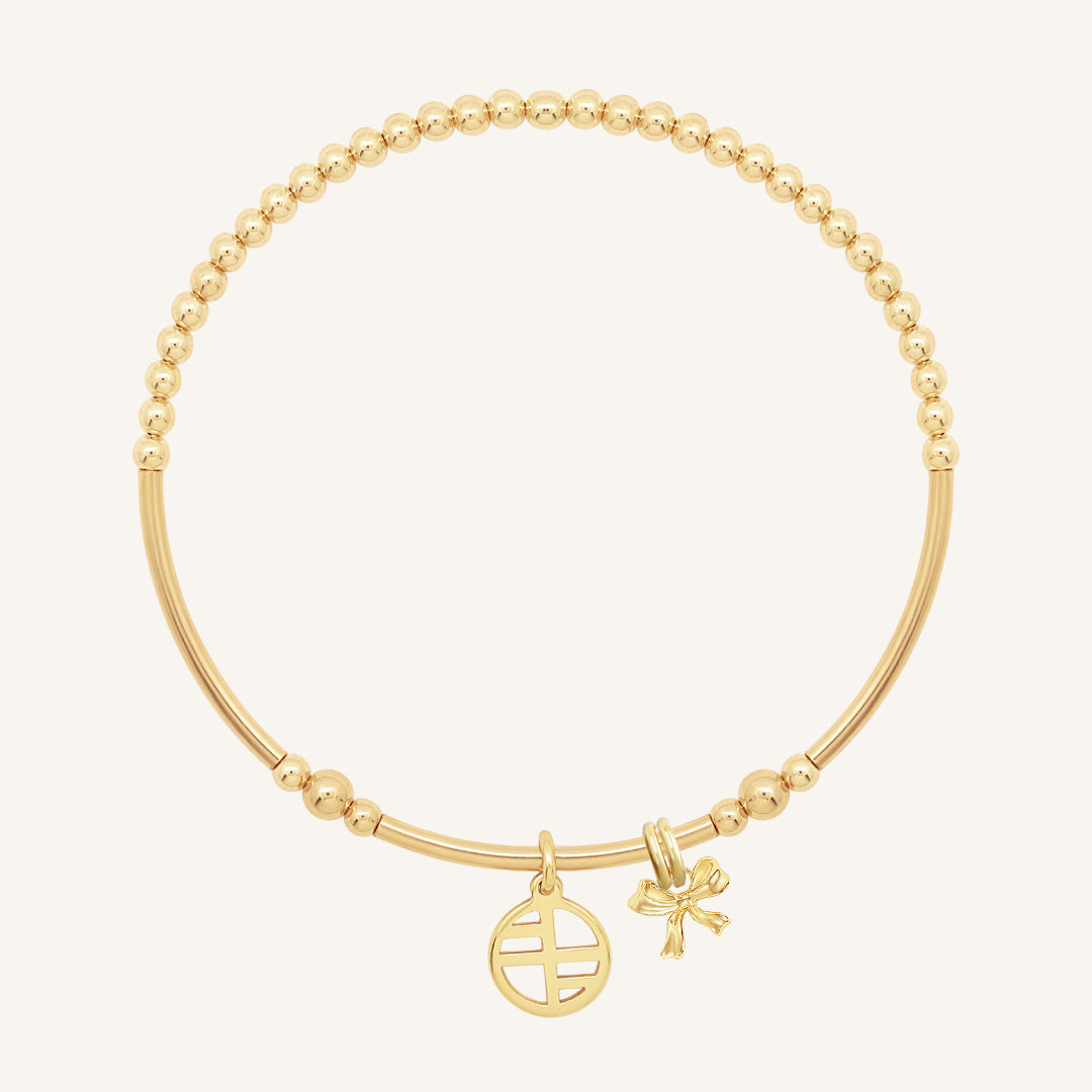 A gold-tone metal bracelet with a beaded design, featuring a charm in the shape of a bow