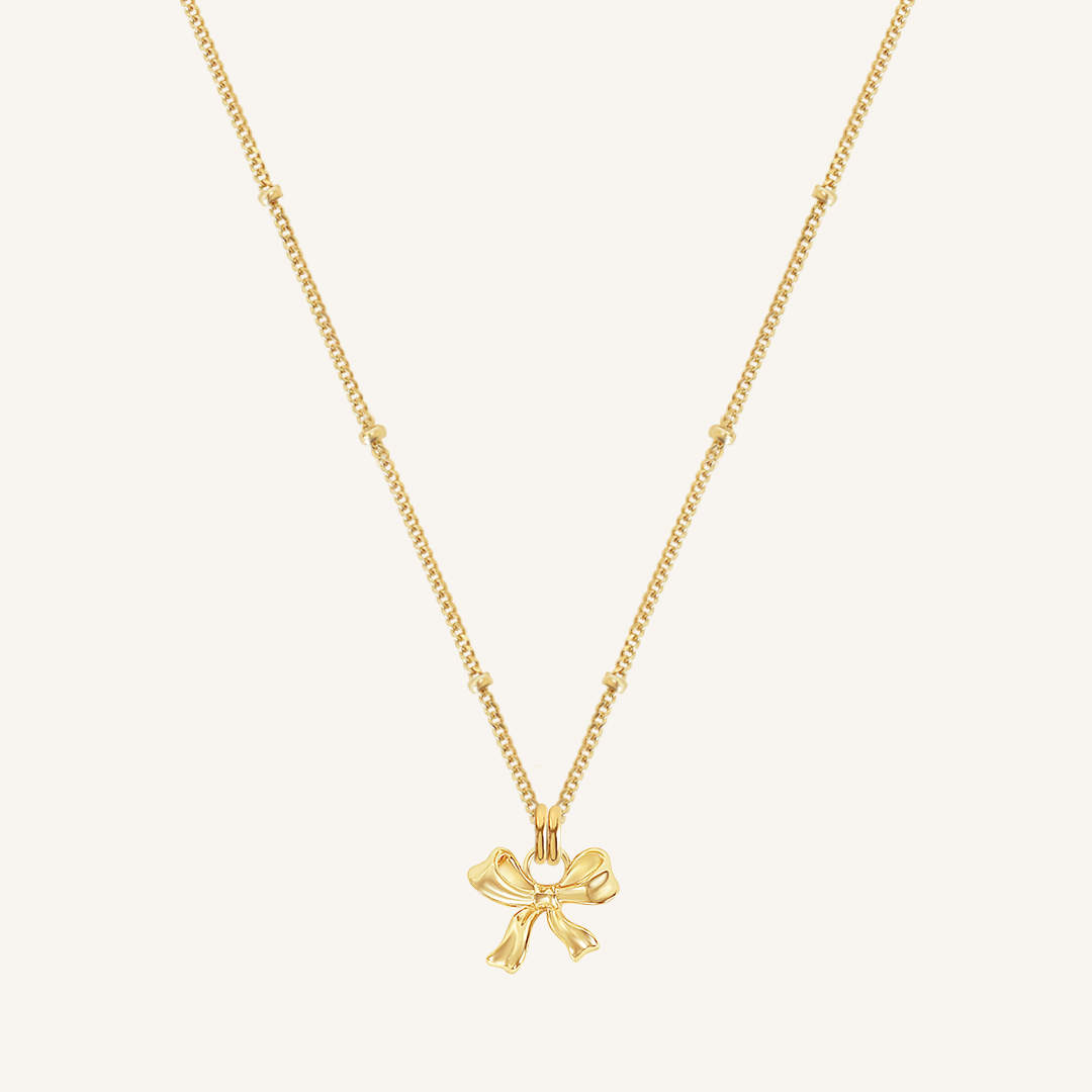 A gold-colored necklace featuring a bow-shaped charm attached to a hoop.
