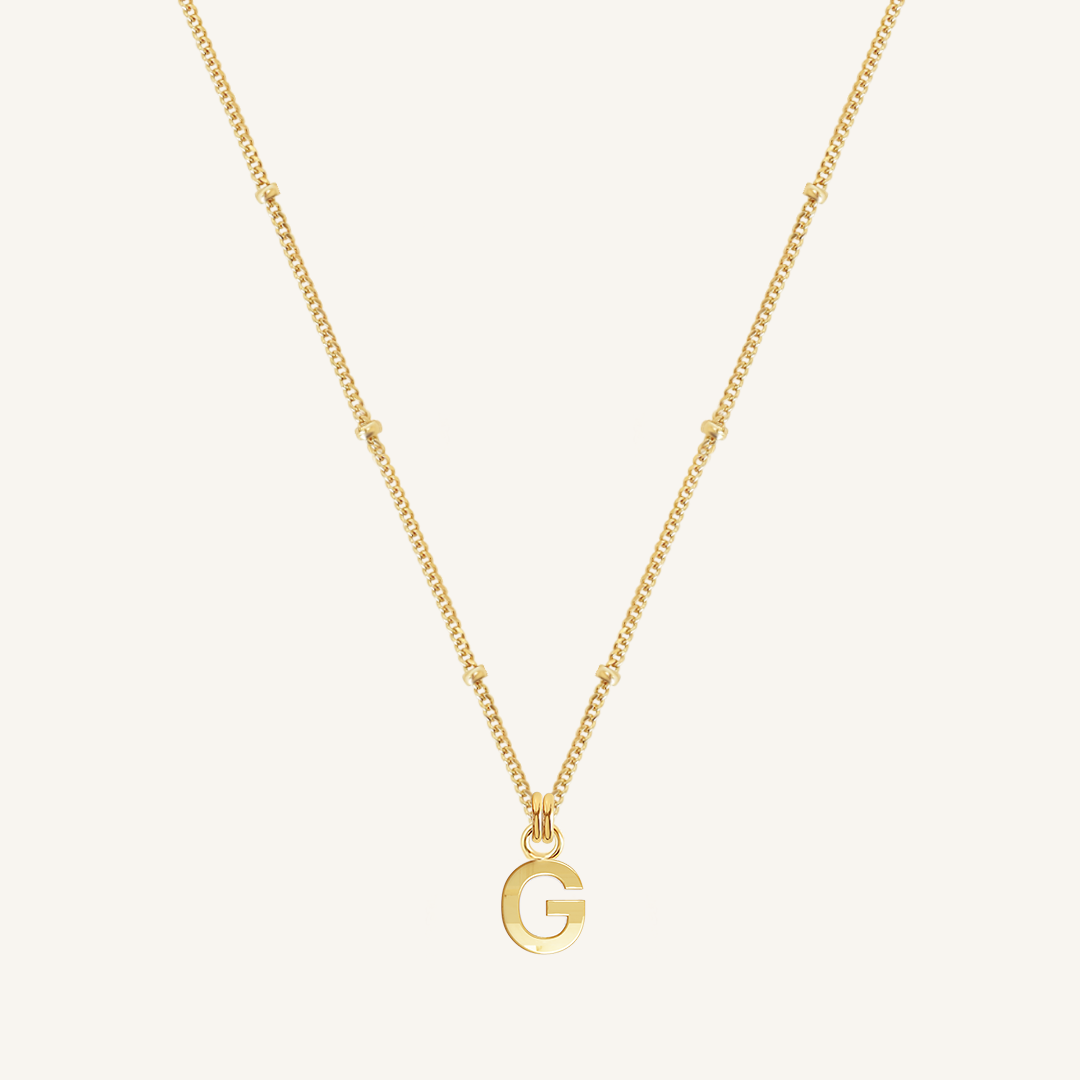 Gold necklace with a 'G' pendant on a light beige background