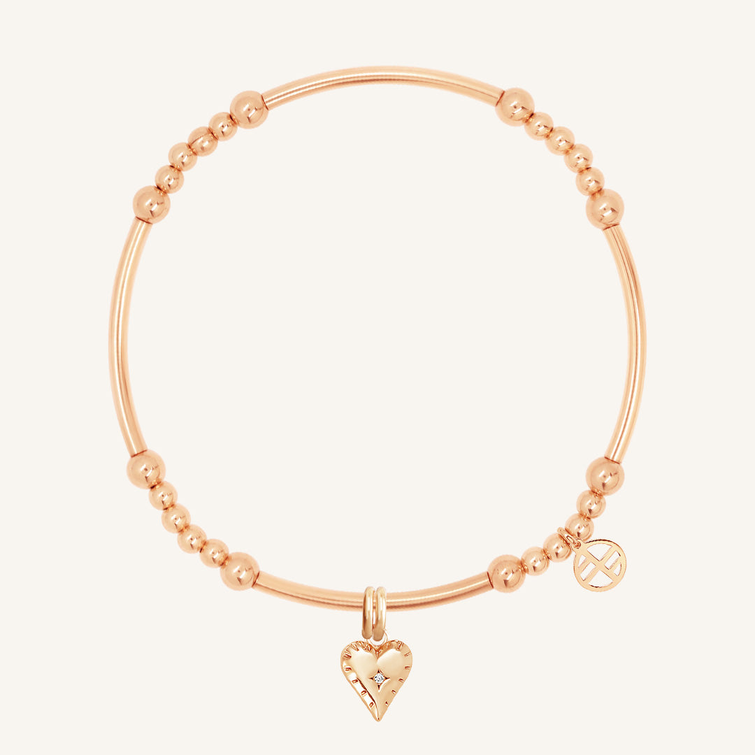 A gold-colored metal bracelet with a heart-shaped charm and small bead details.