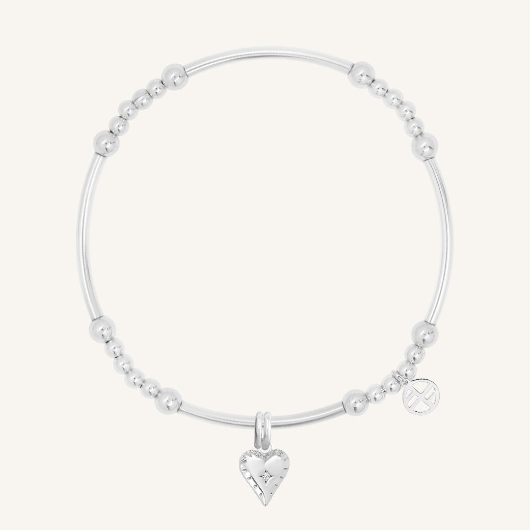 A silver-coloured metal bracelet with a heart-shaped charm and small bead details.
