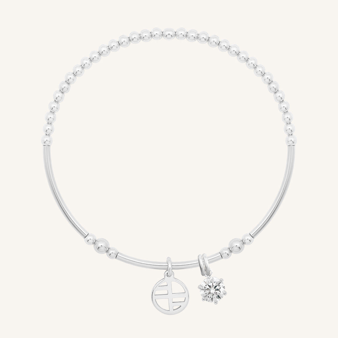 A silver-tone charm bracelet with a beaded design and two charms, one circular and one in the shape of a heart with a small cubic zirconia inside.