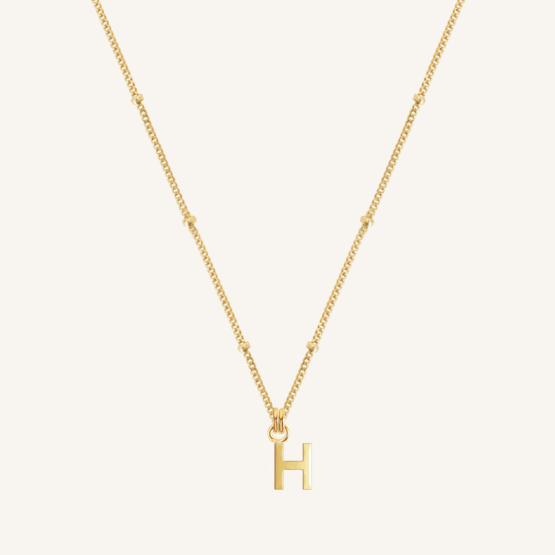 Gold necklace with 'H' pendant on a light beige background