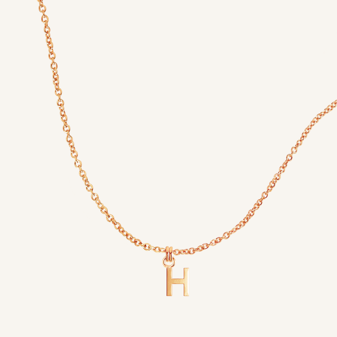 Rose gold necklace with a 'H' pendant on a light beige background