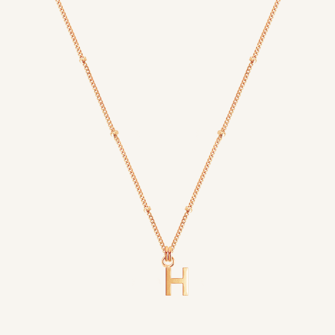 Gold necklace with 'H' pendant on a light beige background