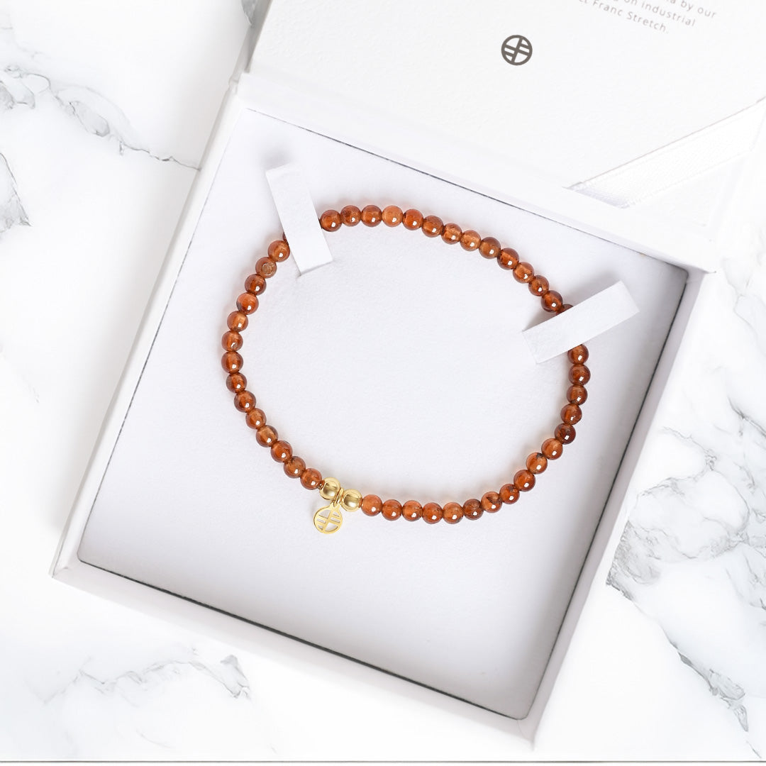 Beaded bracelet with a gold charm on a white box with a marble background