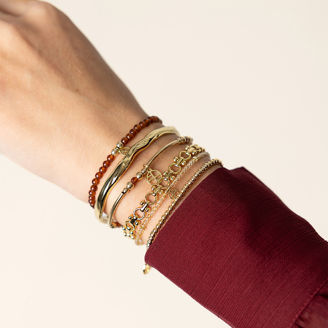 Close-up of a wrist wearing multiple gold bracelets on a plain background