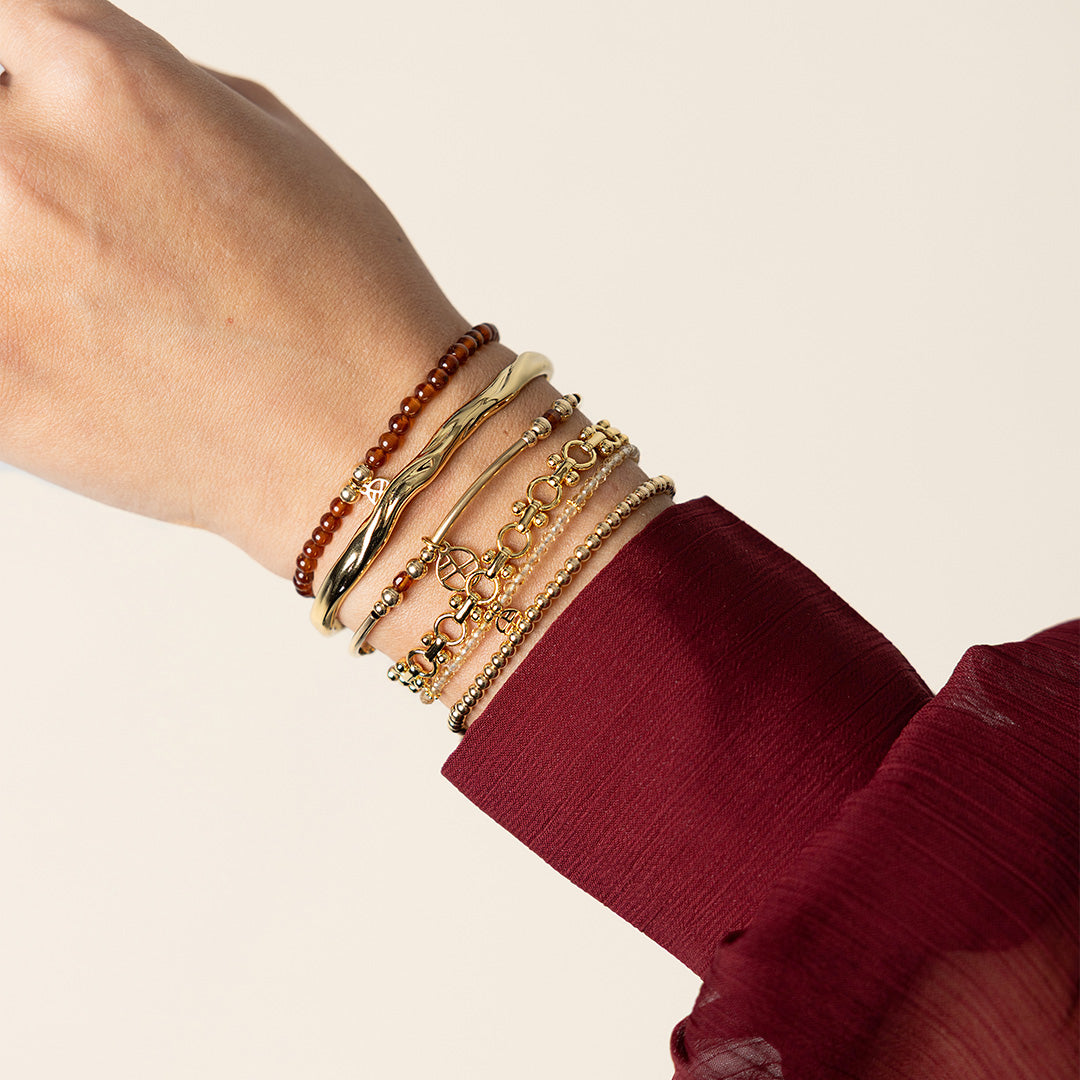 Close-up of a wrist wearing multiple gold bracelets on a beige background