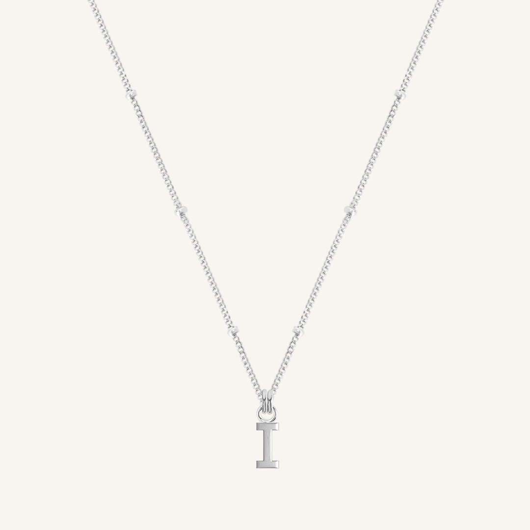 Silver necklace with a 'I' pendant on a light gray background