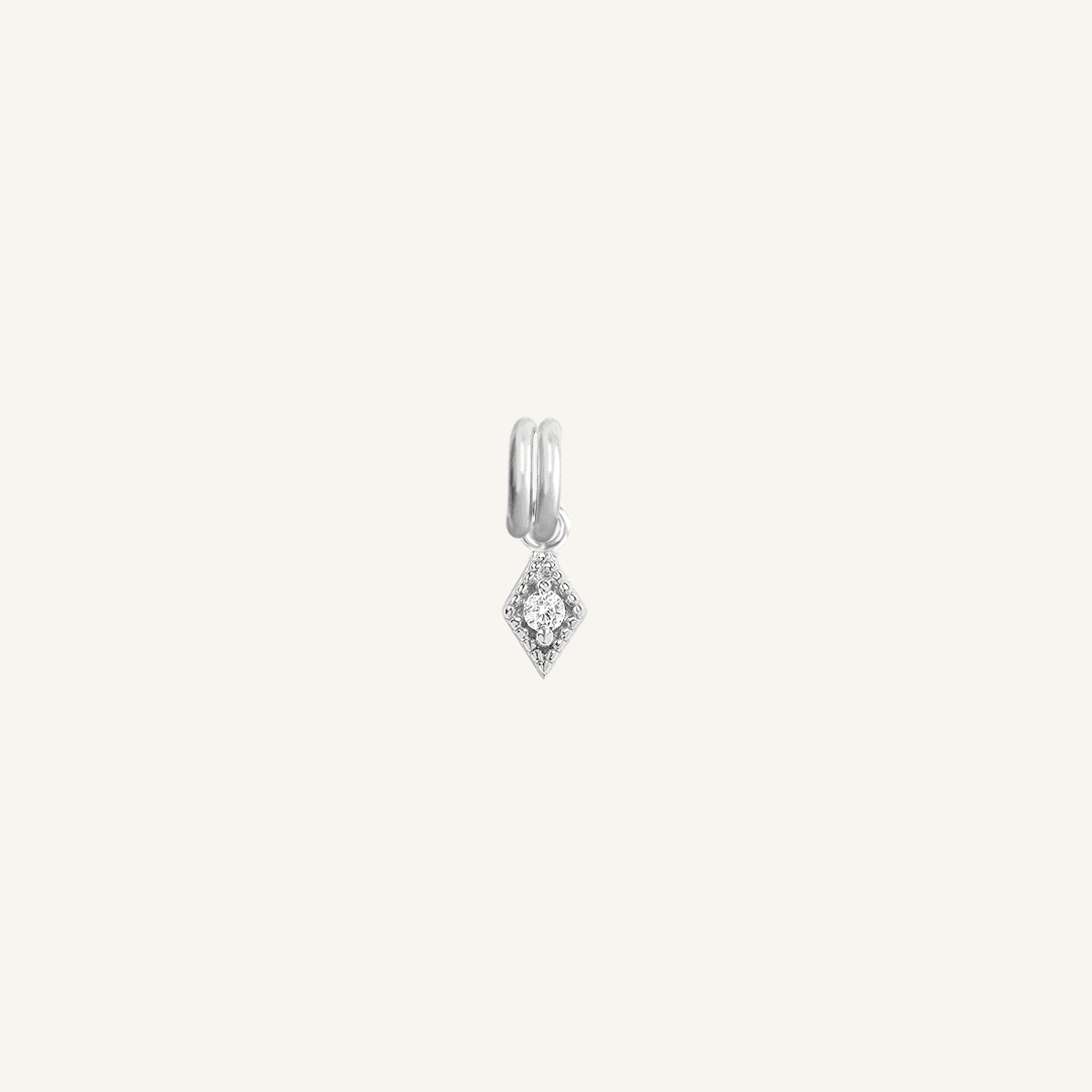 A small silver-colored charm with a diamond-shaped design on a plain background.