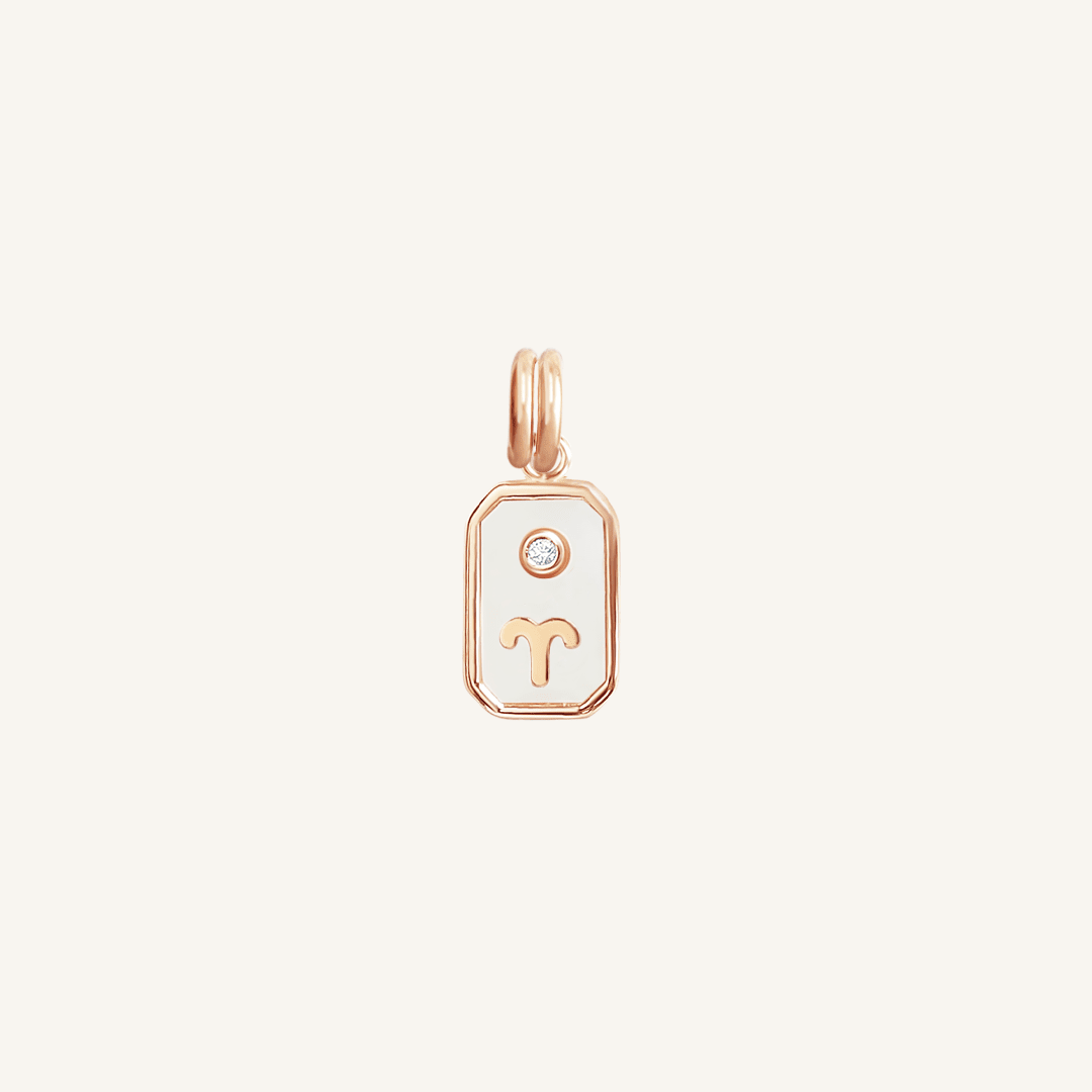A rose gold rectangular shaped charm with the Aries zodiac symbol on it, designed with an iridescent finish.