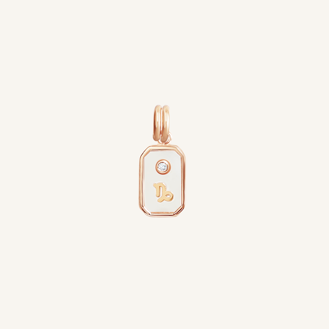 A rose gold rectangular shaped charm with the Capricorn zodiac symbol on it, designed with an iridescent finish.