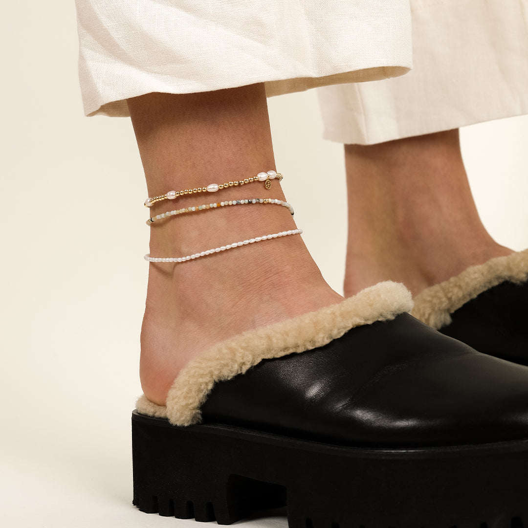 A coloured stretchy anklet with freshwater pearls and a small gold charm, worn on the ankle