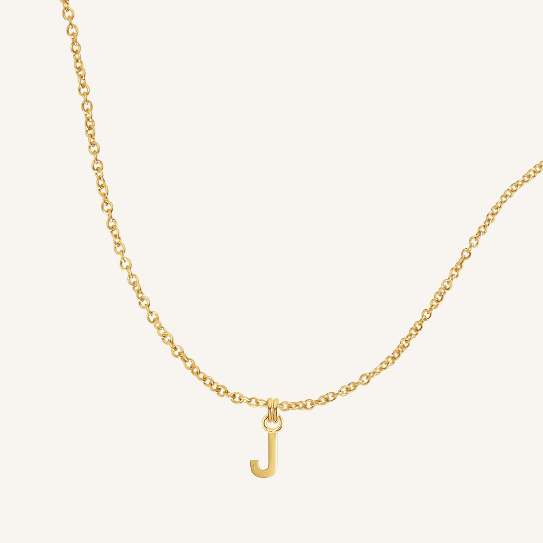 Gold necklace with a 'J' pendant on a light beige background