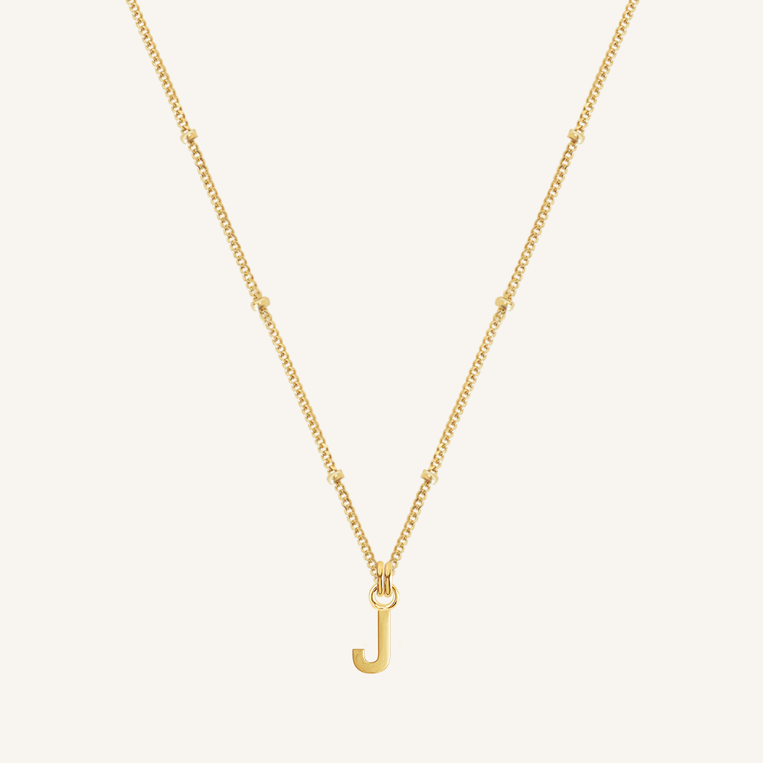 Gold necklace with a 'J' pendant on a light beige background