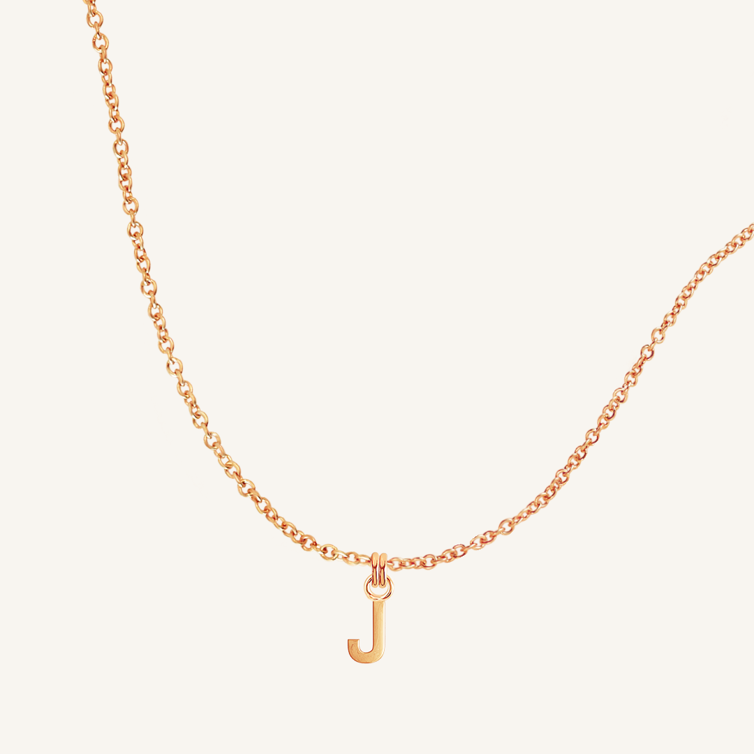 Rose gold necklace with a 'J' pendant on a light beige background