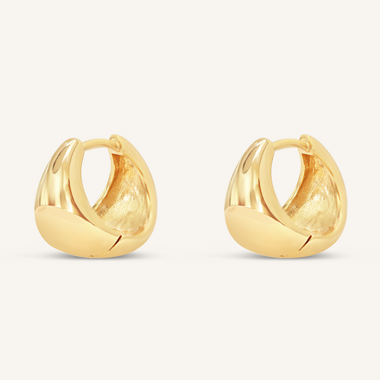 A pair of gold-colored huggie hoop earrings on a white background.
