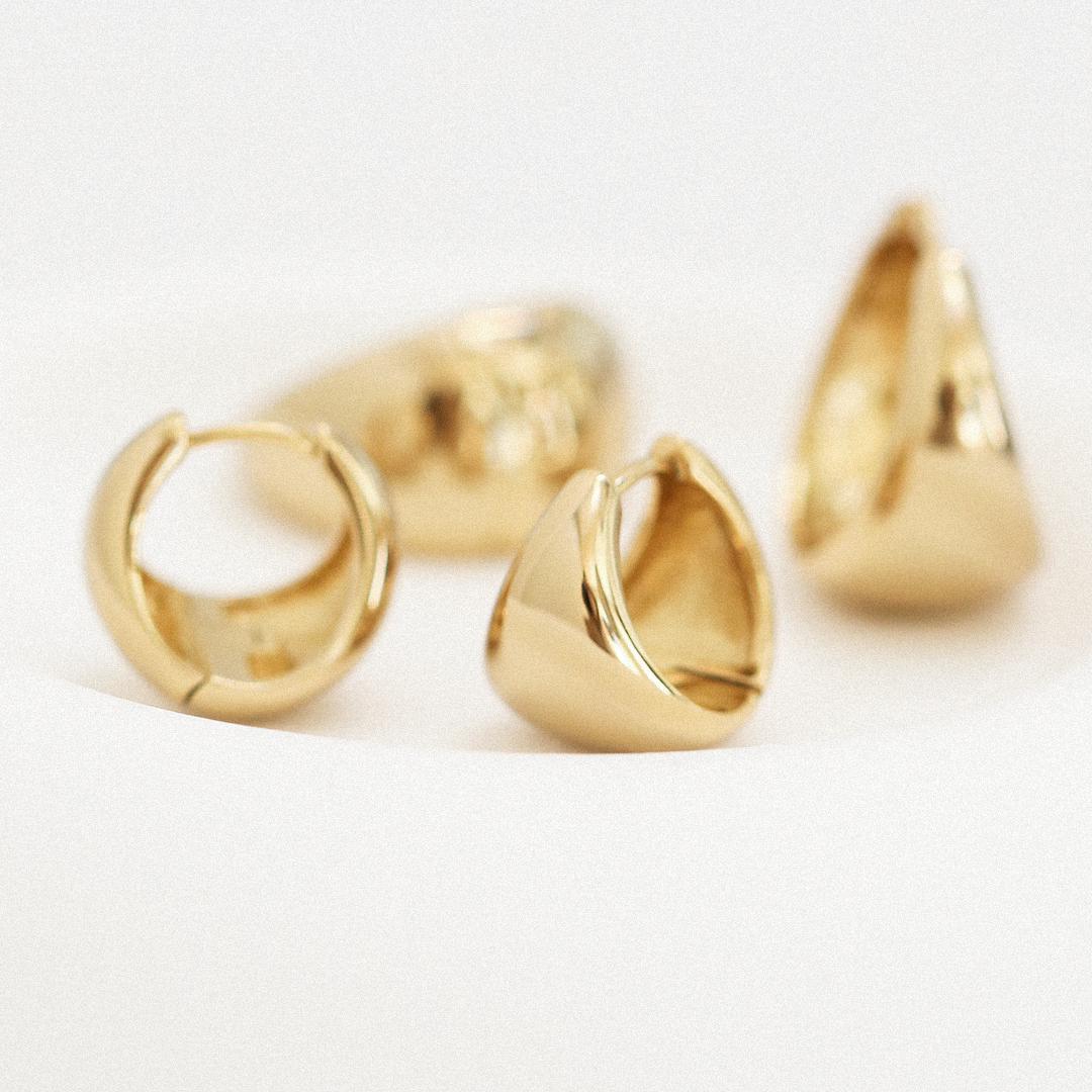 A pair of gold-colored huggie hoop earrings on a white background.