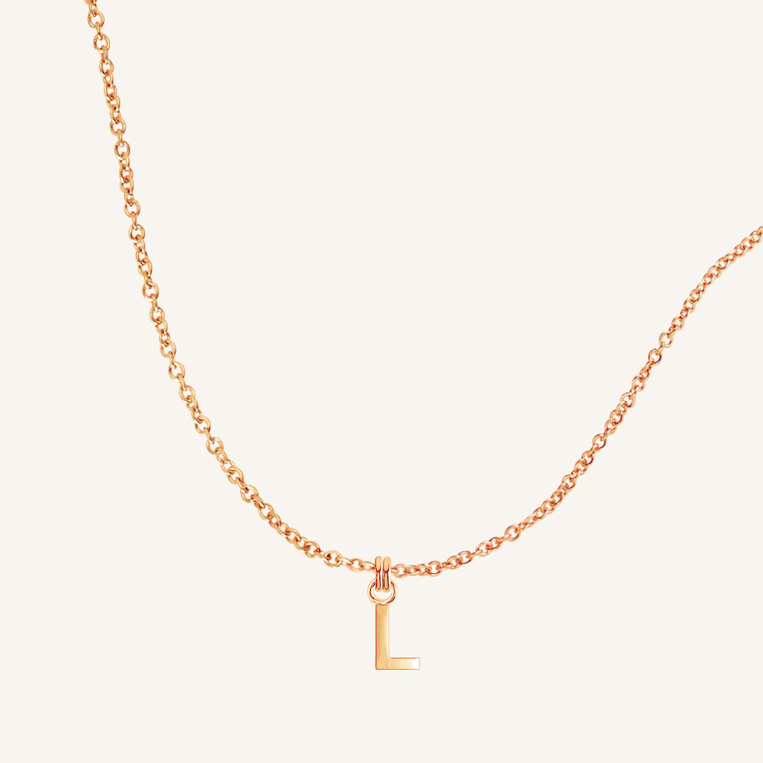 Rose gold necklace with a 'L' pendant on a light beige background