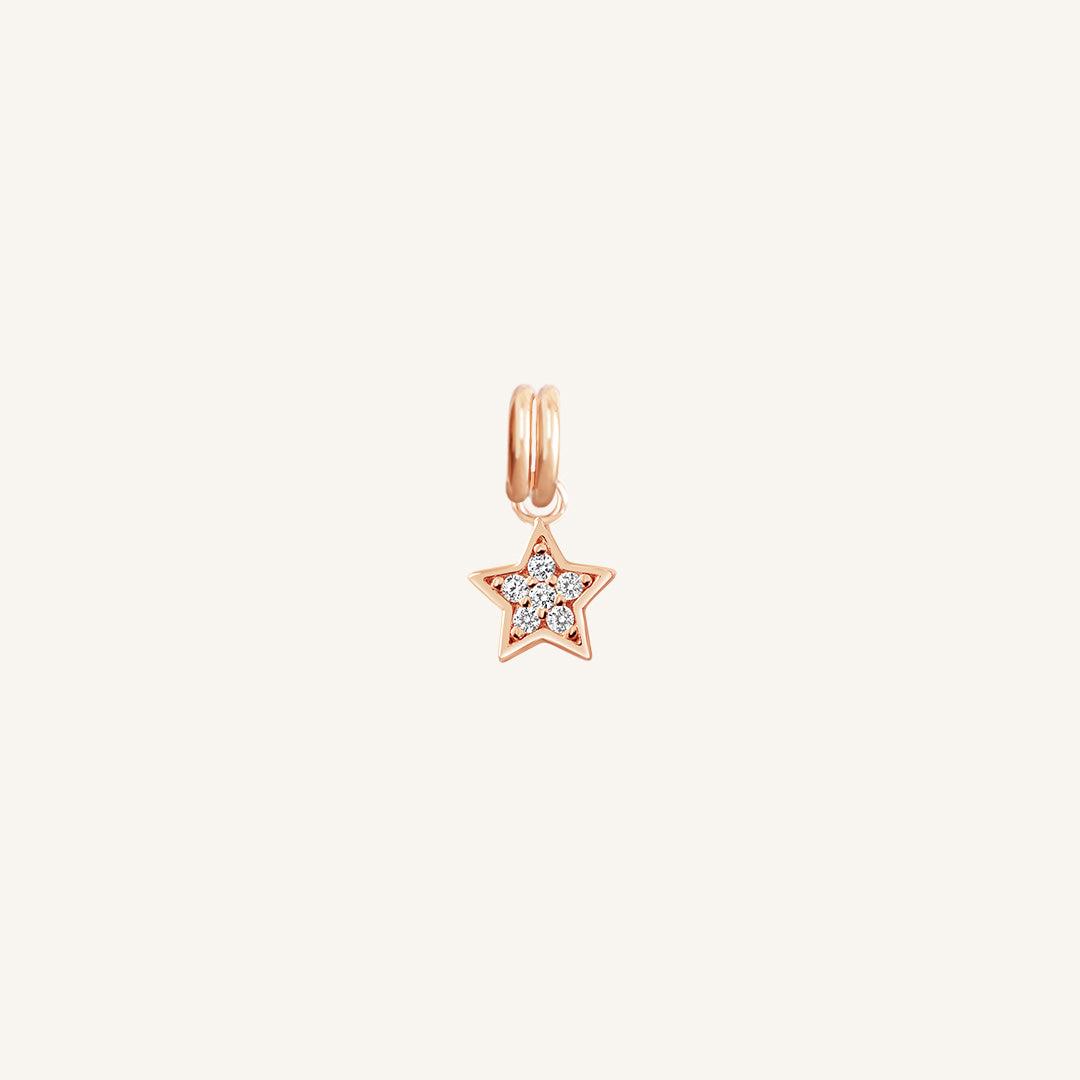 A rose gold coloured charm in the shape of a star with a small cubic zirconias, designed to be attached to a bracelet or chain.