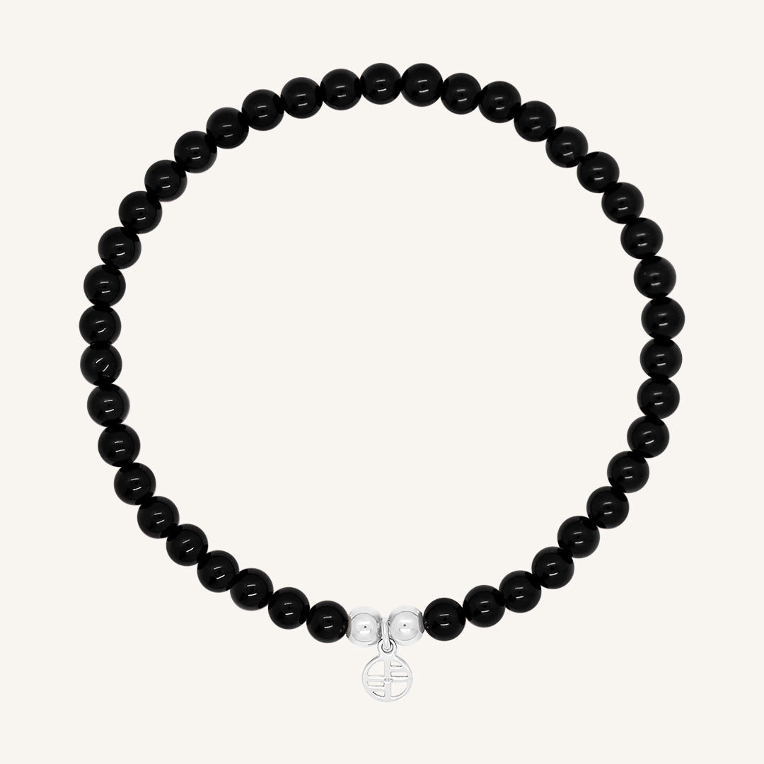 A black beaded bracelet made of black agate stones with a silver charm, displayed against a white background.