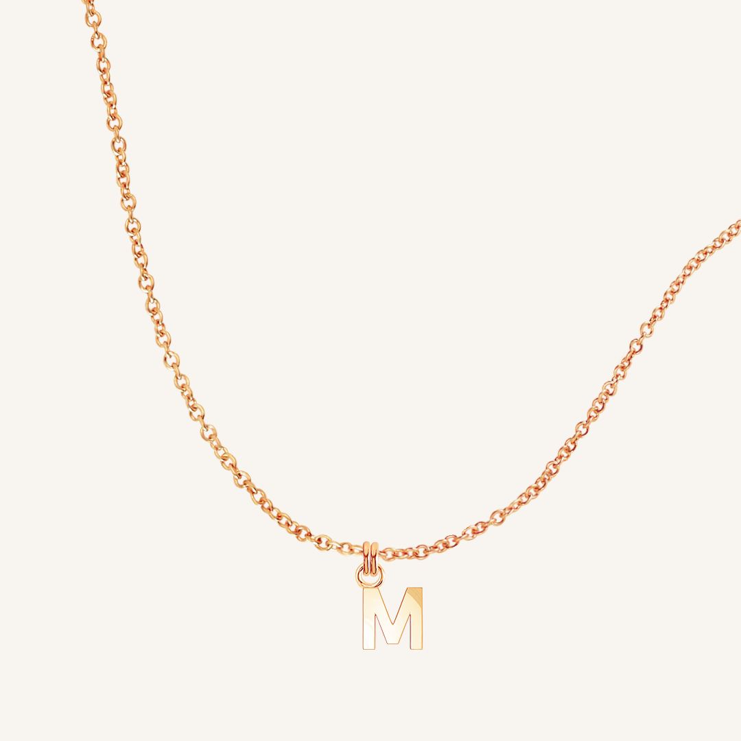 Rose gold necklace with a 'M' pendant on a light beige background