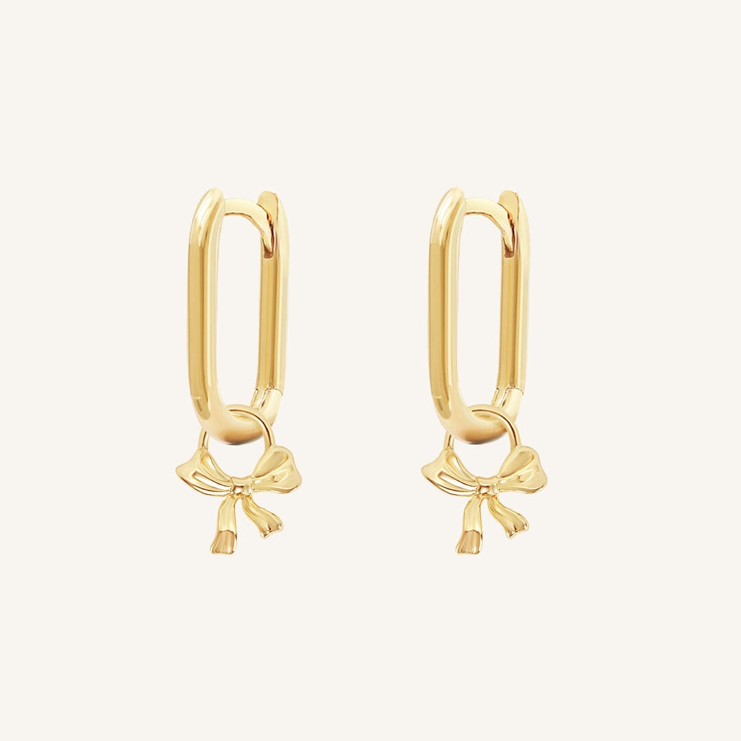 A pair of gold-tone hoop earrings with a charm in the shape of a rectangle bow.