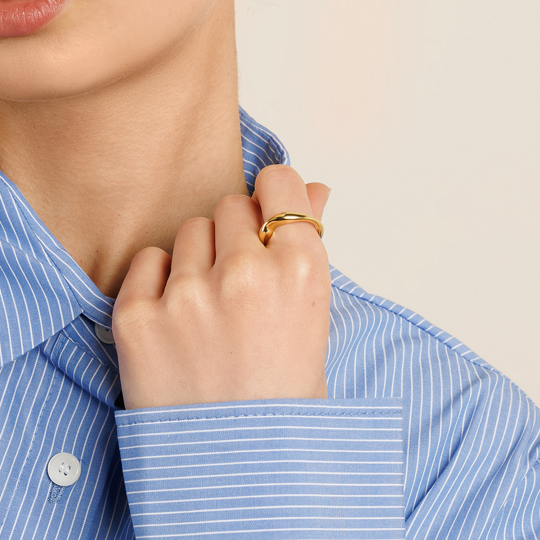 A gold-coloured ring with an irregular, smooth shape worn on finger