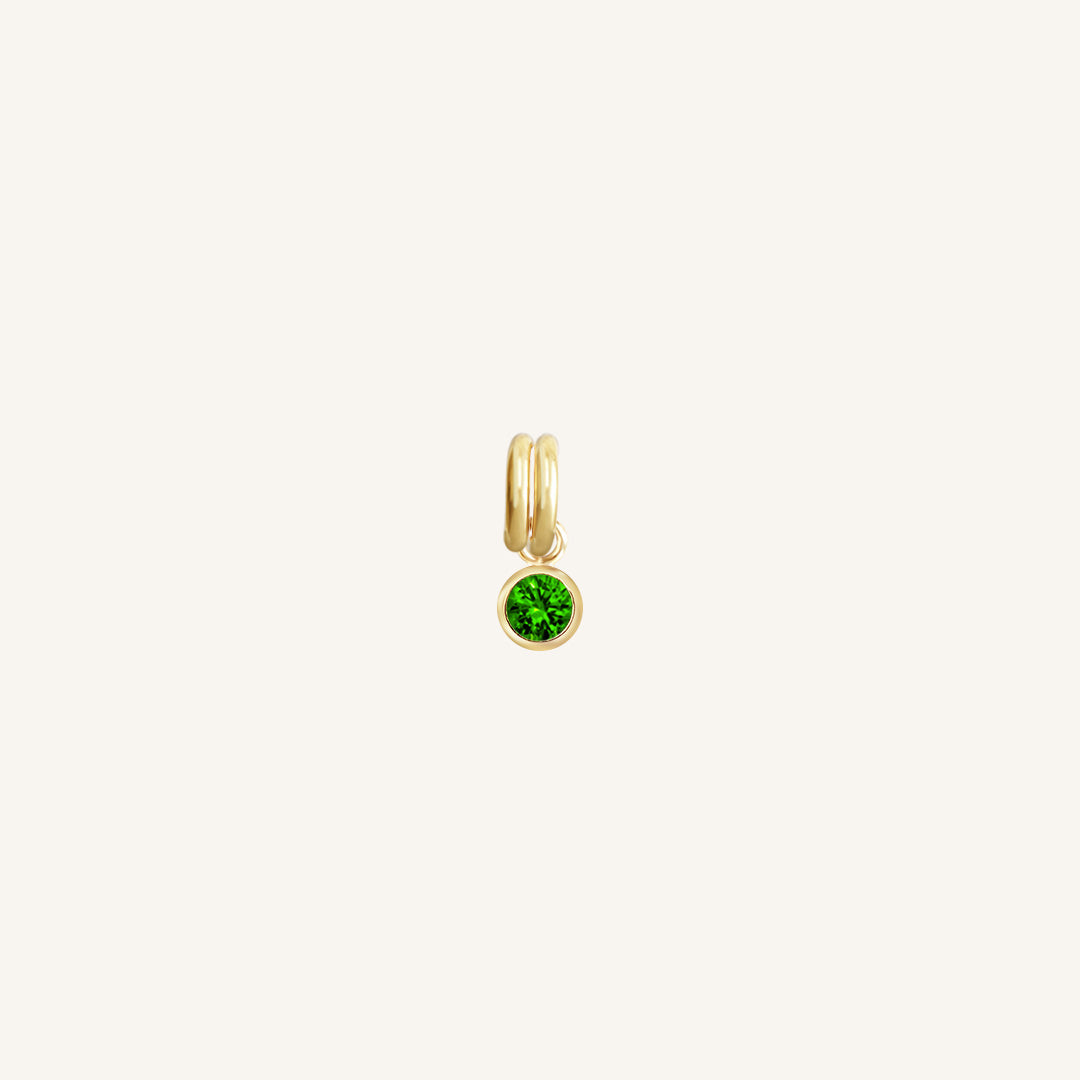A gold, round bezel set emerald cubic zirconia reflects May birthstone colour