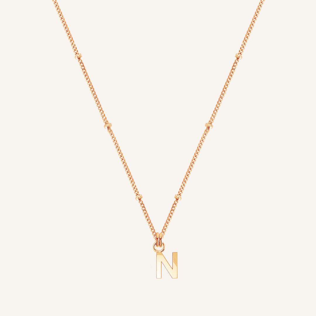 Rose gold necklace with a 'N' pendant on a light pink background