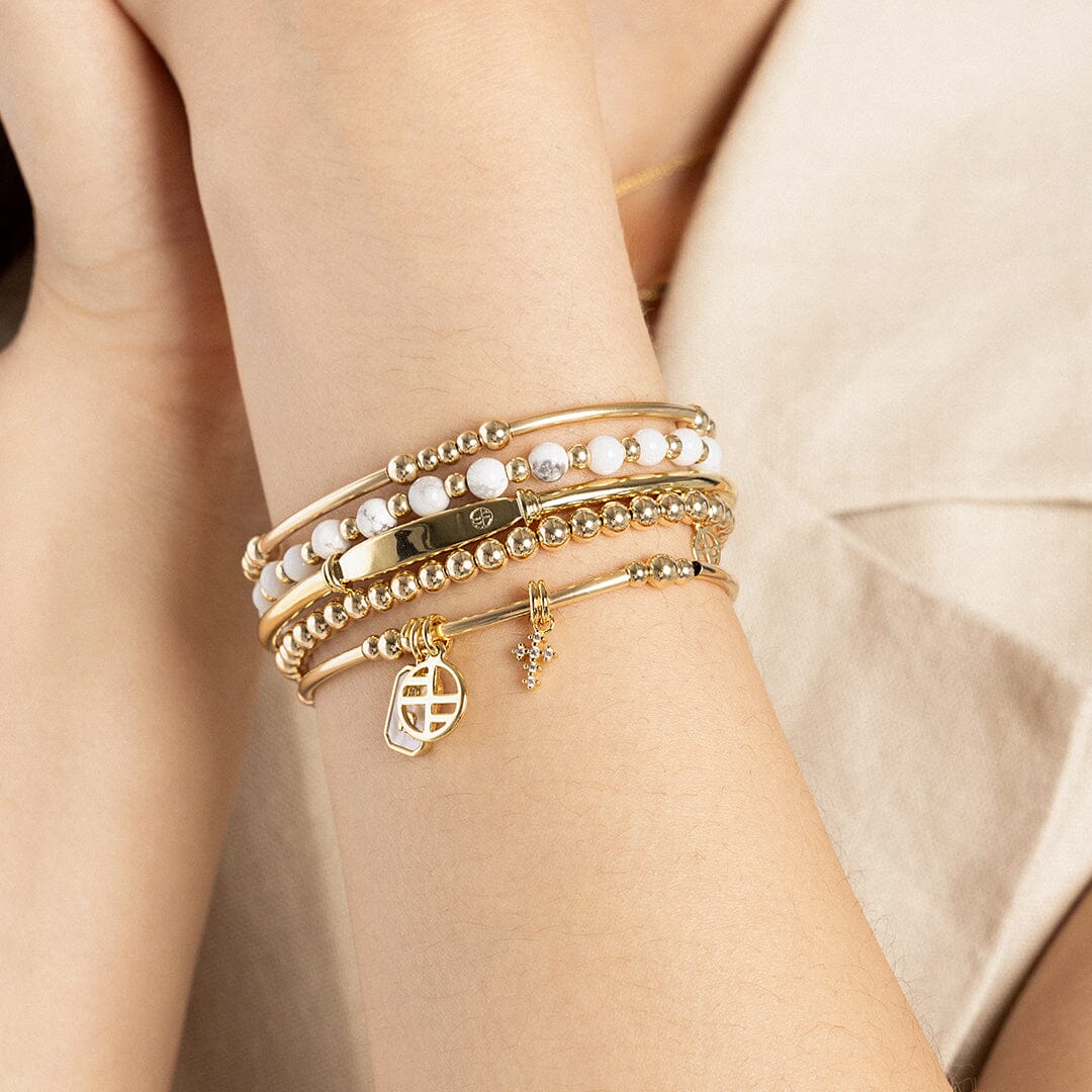 A petite gold cross charm with cubic zirconia attached to bracelet, on wrist
