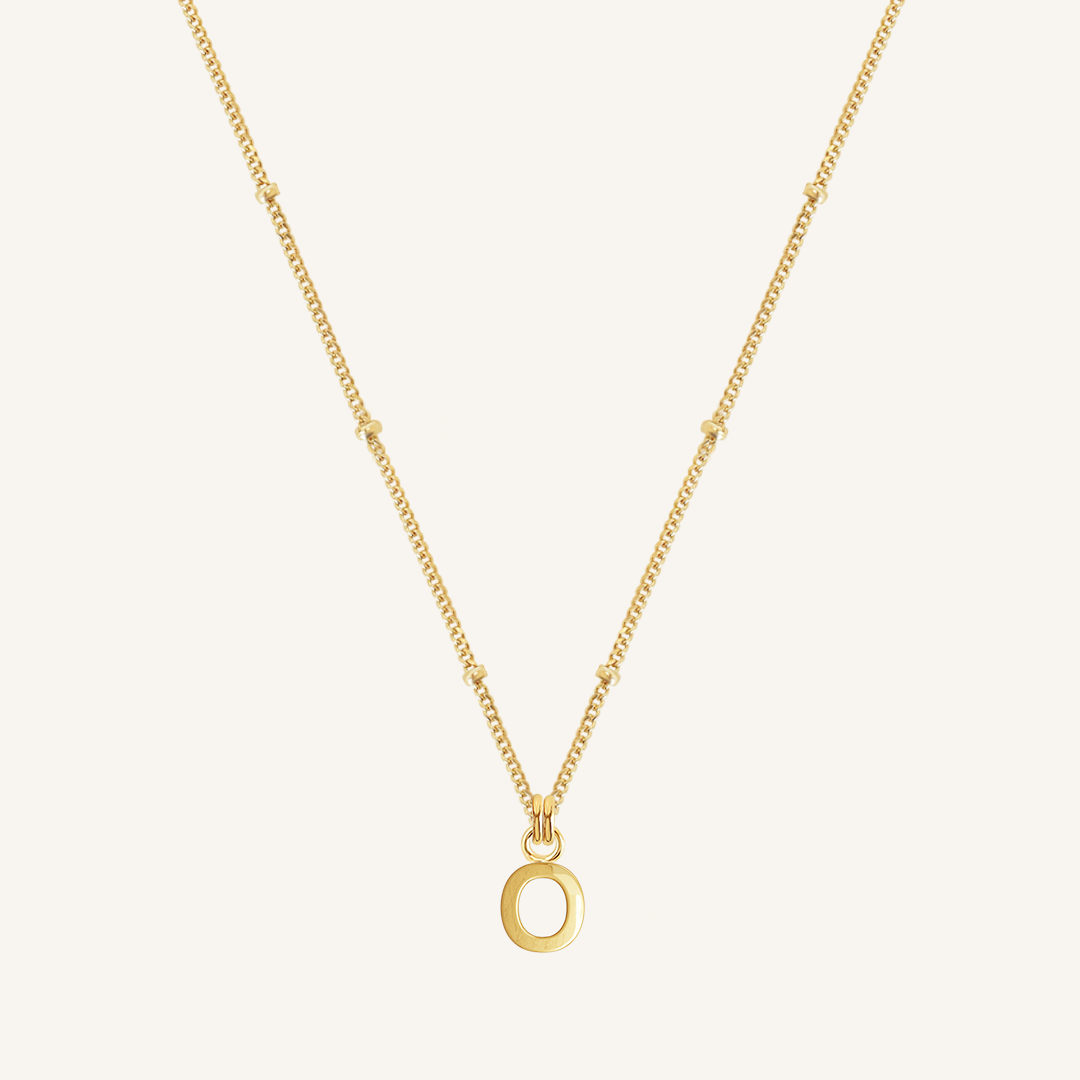 Gold necklace with an O pendant on a light beige background