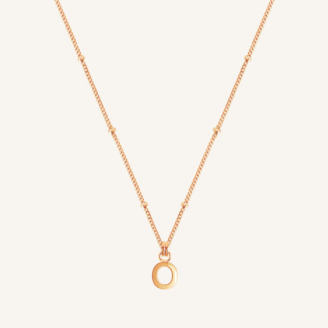 Rose gold necklace with an 'O' pendant on a light beige background
