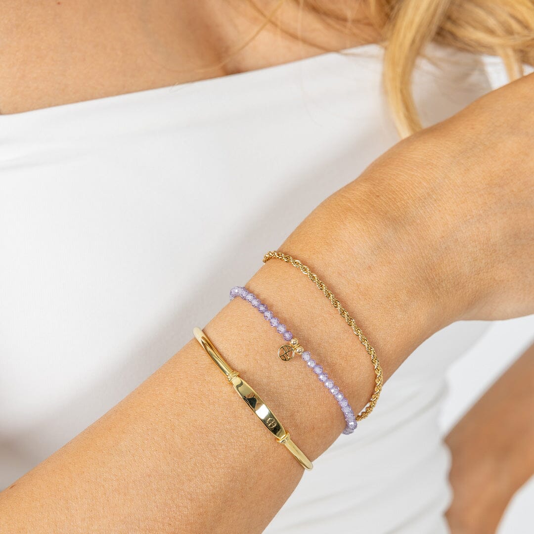 Close-up of a person's wrist wearing multiple gold and beaded bracelets on a white background