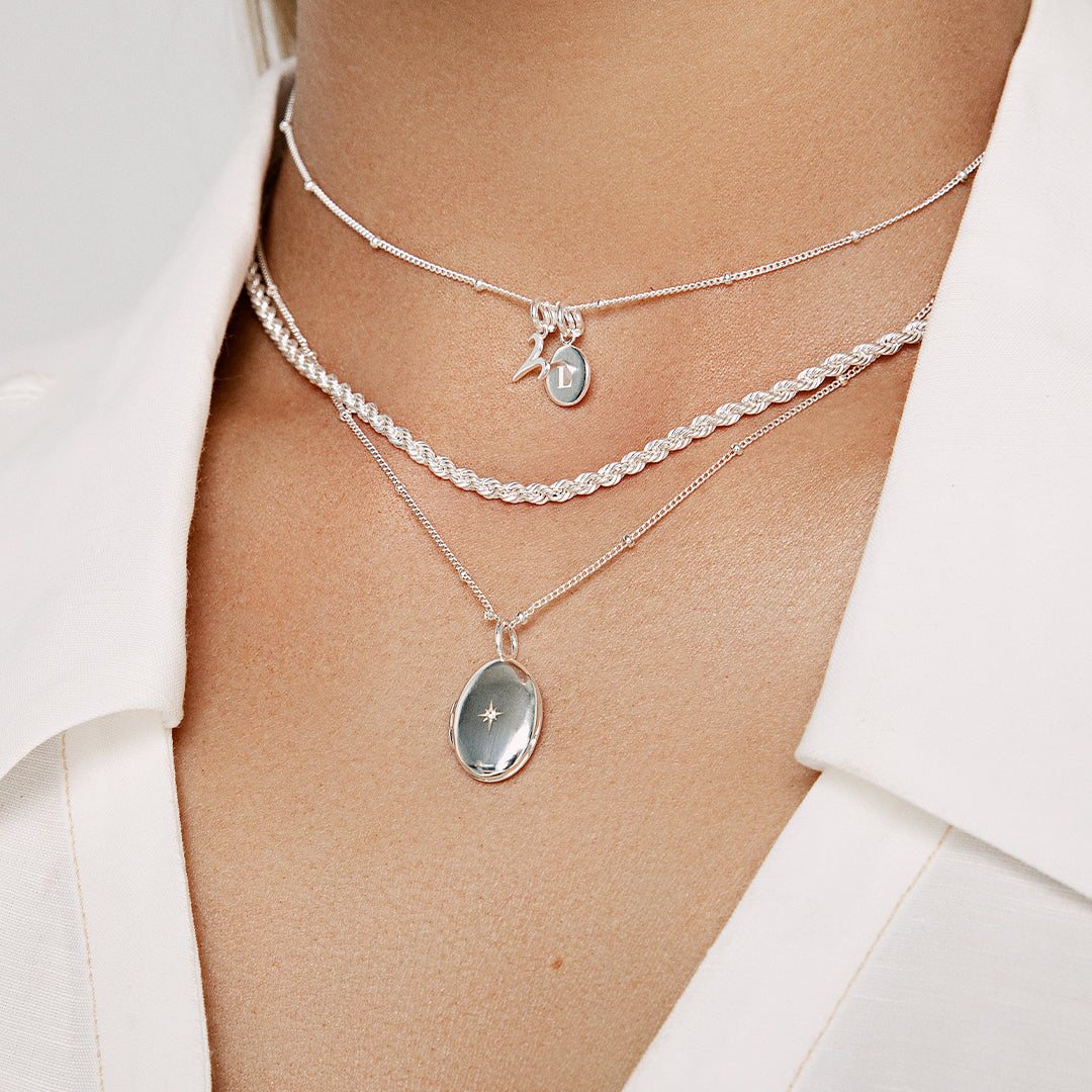 An oval-shaped photo locket with a silver metal tone, on chain, around neck