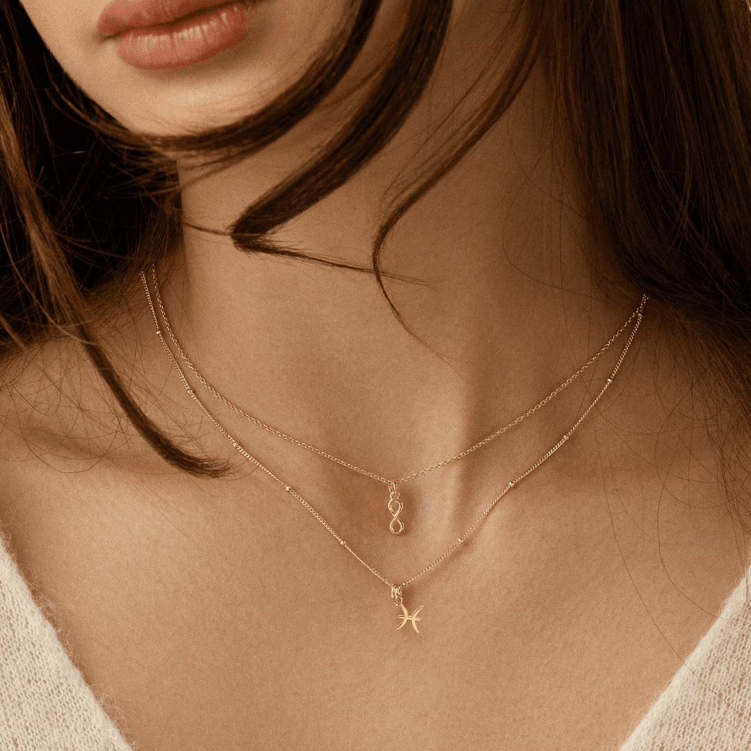 A gold-coloured Petite Zodiac Charm representing the Pisces sign on a chain around the neck