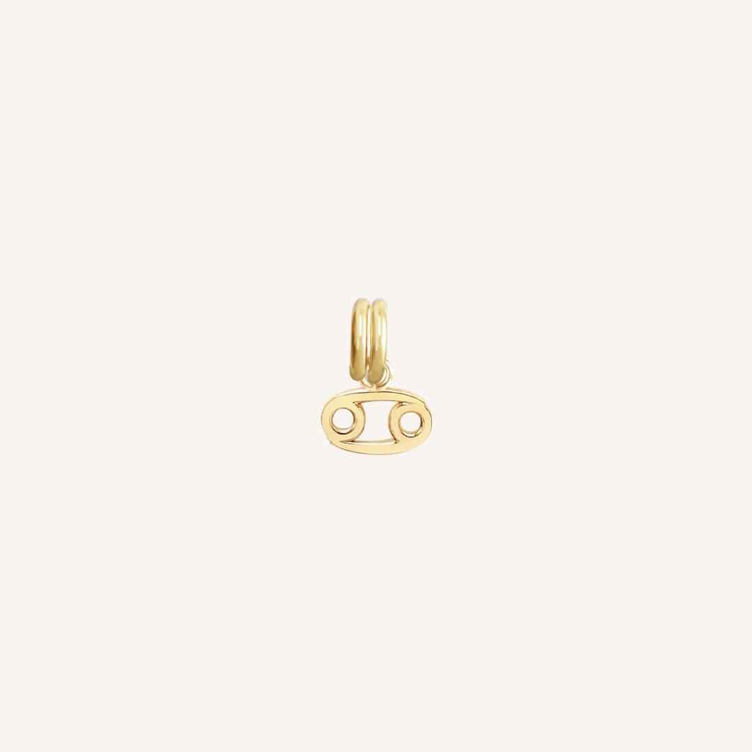 A small gold charm with the symbol for the zodiac sign Cancer.
