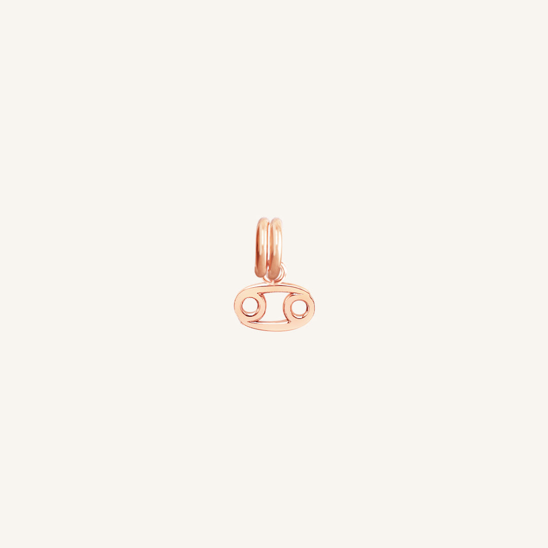A small rose gold charm with the symbol for the zodiac sign Cancer.