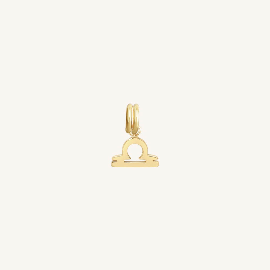 A gold charm in the shape of the Libra zodiac symbol.