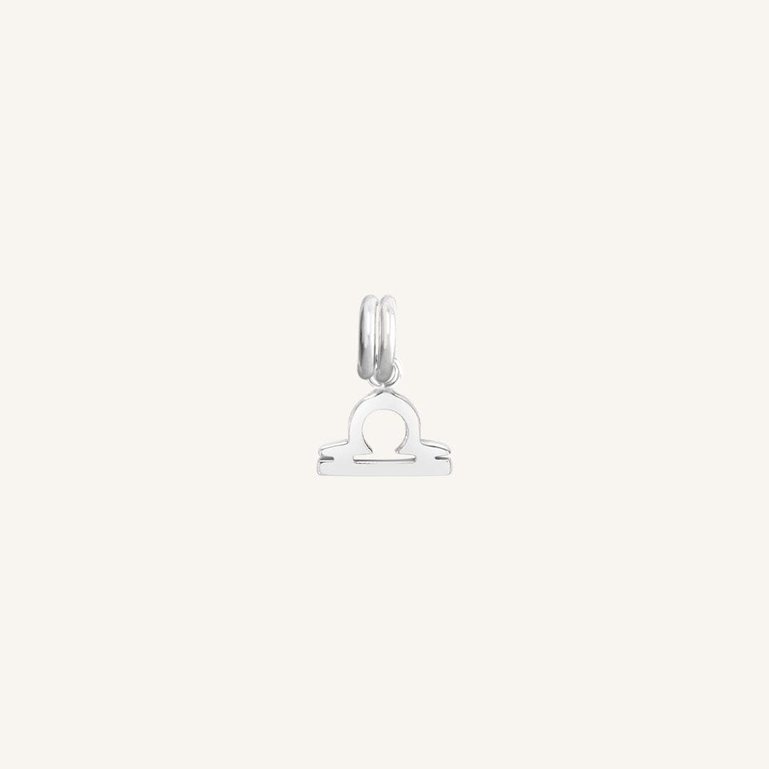 A silver charm in the shape of the Libra zodiac symbol.