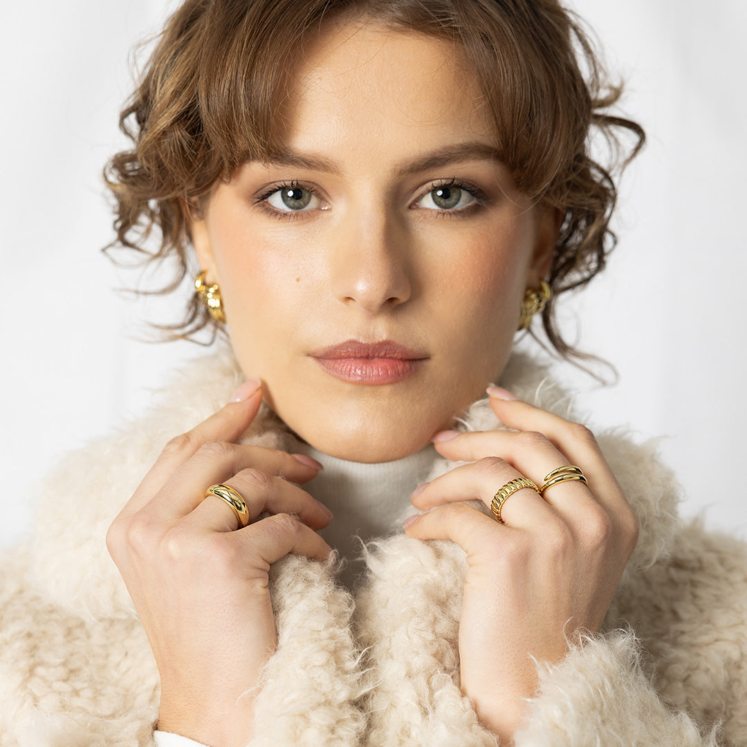 Woman wearing gold earrings and rings with a white fur coat on a light background
