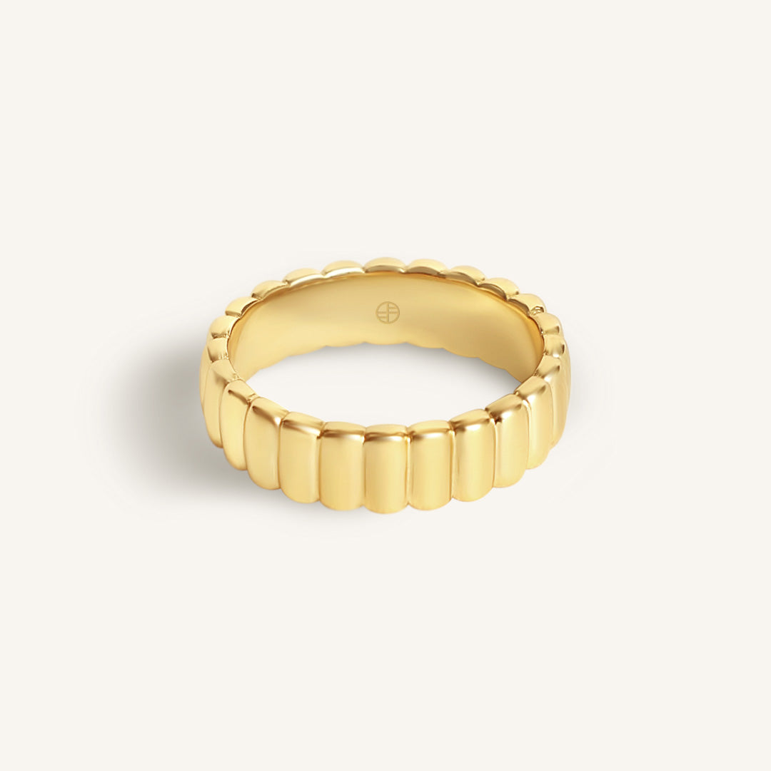 Gold ring with a textured band on a light beige background